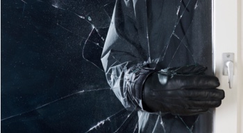 A criminal's hand reaching into broken window to unlock it