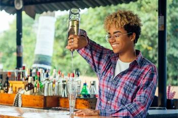 bartender pouring alcohol into glass in sunny outdoor bar area