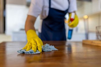 Person with rubber gloves cleaning table with cloth