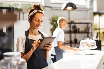 smiling woman behind bakery counter looking at digital tablet