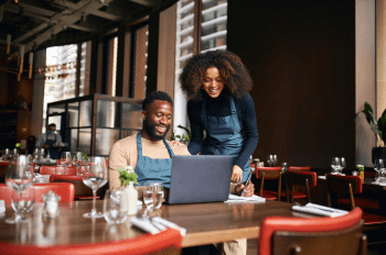 Restaurant managers smiling working with laptop inside of restaurant before business hours