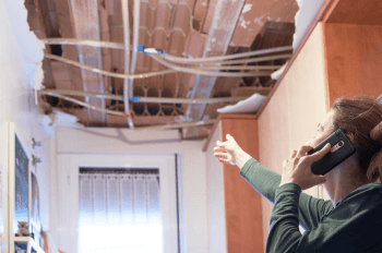 Woman on phone pointing at collapsed ceiling in home
