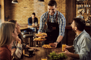 Smiling waiter serving restaurant guests plates of burgers and fries