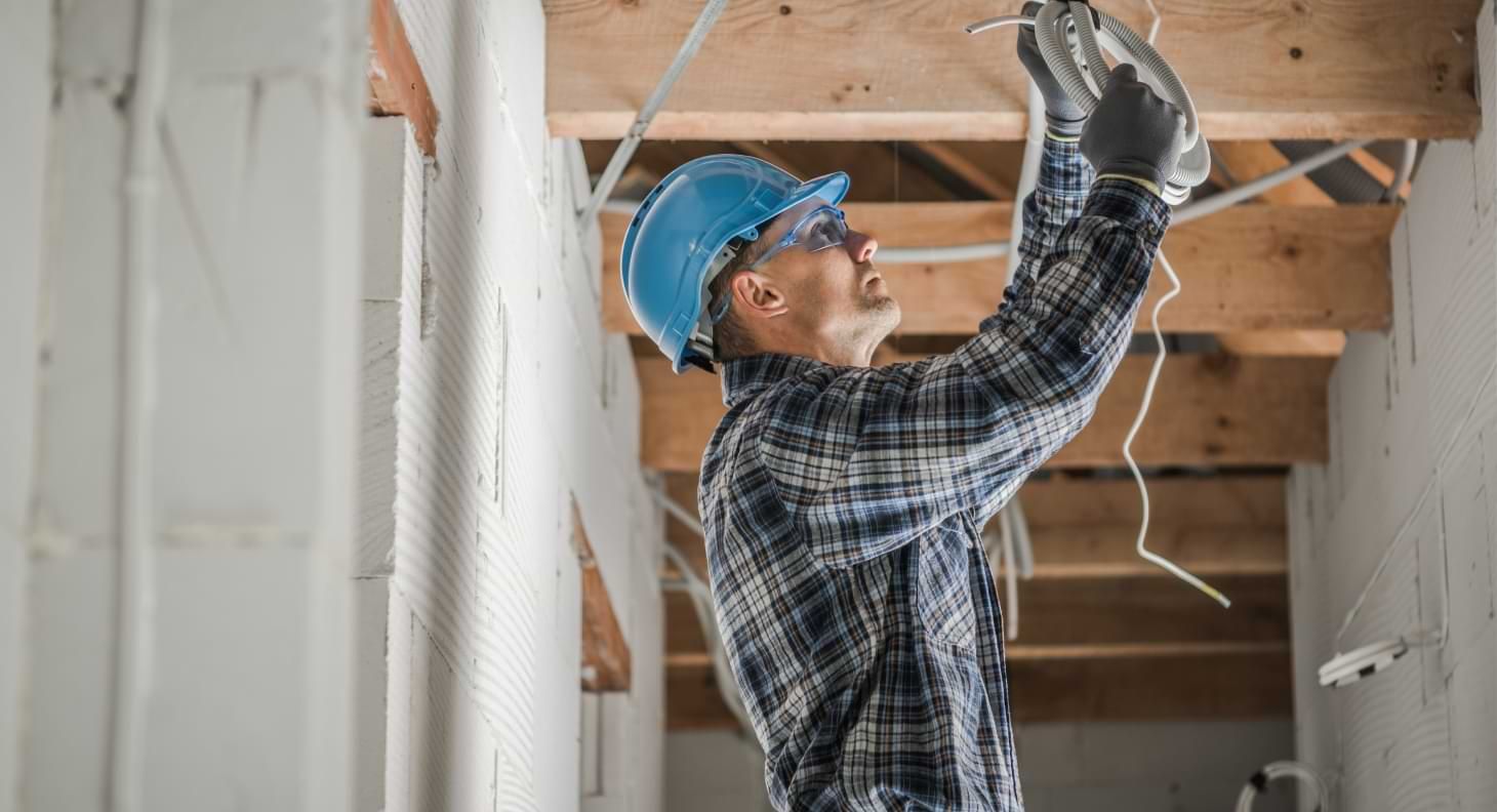 Man wearing blue hardhat fixing electrical wiring in ceiling