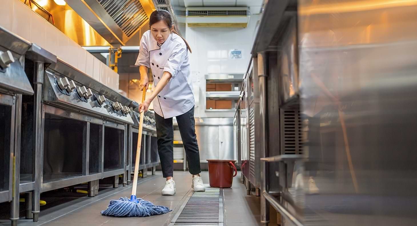 Woman mopping floor in industrial kitchen