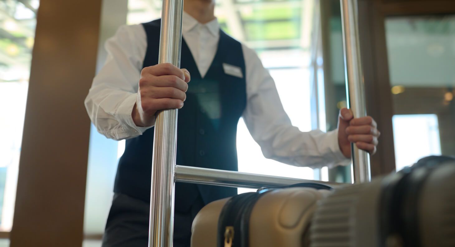 Hotel employee pushing a luggage cart containing suitcases