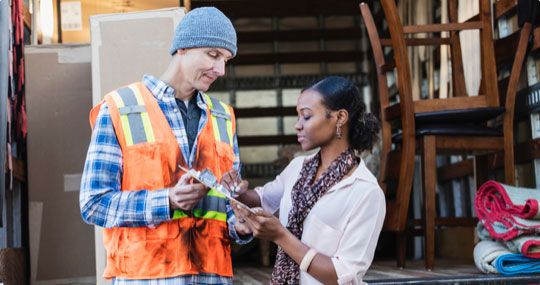 Man wearing hi-vis construction vest handing woman in businesswear clipboard to sign