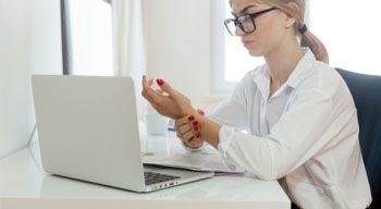 woman sitting at desk with laptop rubbing wrist