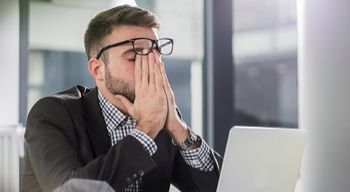 stressed man sitting at desk in office with his head in his hands