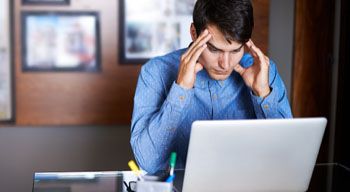 distressed man looking at laptop rubbing temples