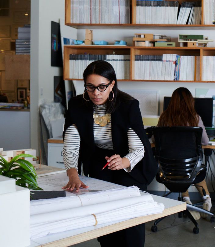 woman in office writing on blueprints with red pencil