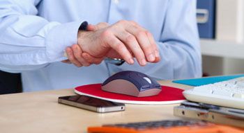 man rubbing sore wrist with hand hovering over computer mouse