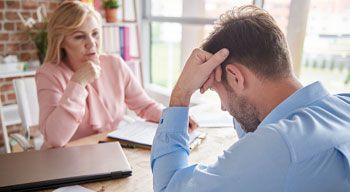 man holding head in his hands speaking with woman in office