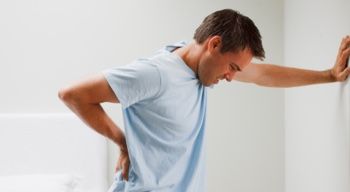 man leaning against wall rubbing lower back