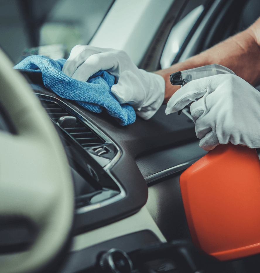 Man wearing gloves spraying car dashboard with cleaner, wiping it off with rag