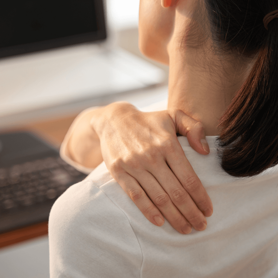 Woman sitting at computer desk rubbing her aching shoulder