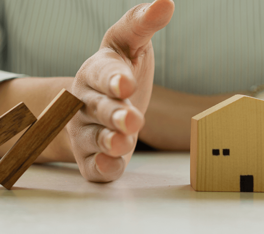 Hand stopping wooden blocks from toppling over onto wooden house