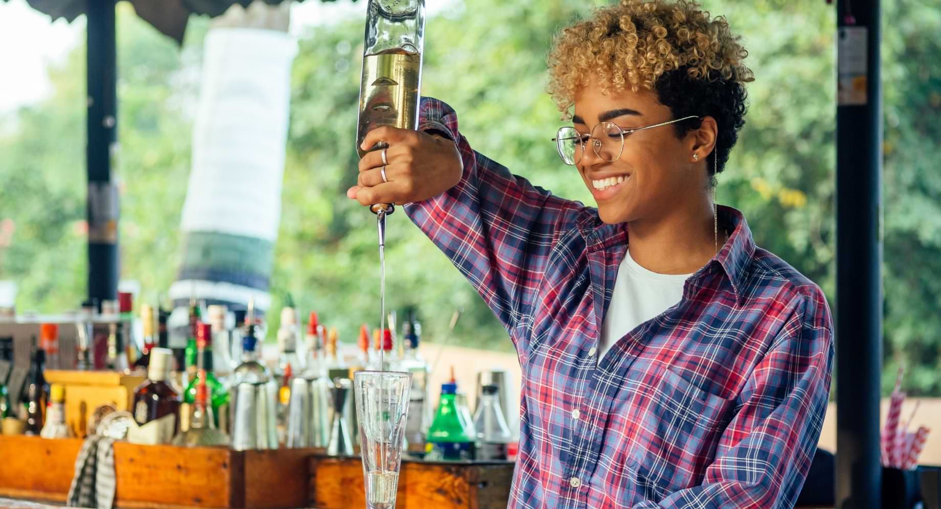 bartender pouring alcohol into glass in sunny outdoor bar area