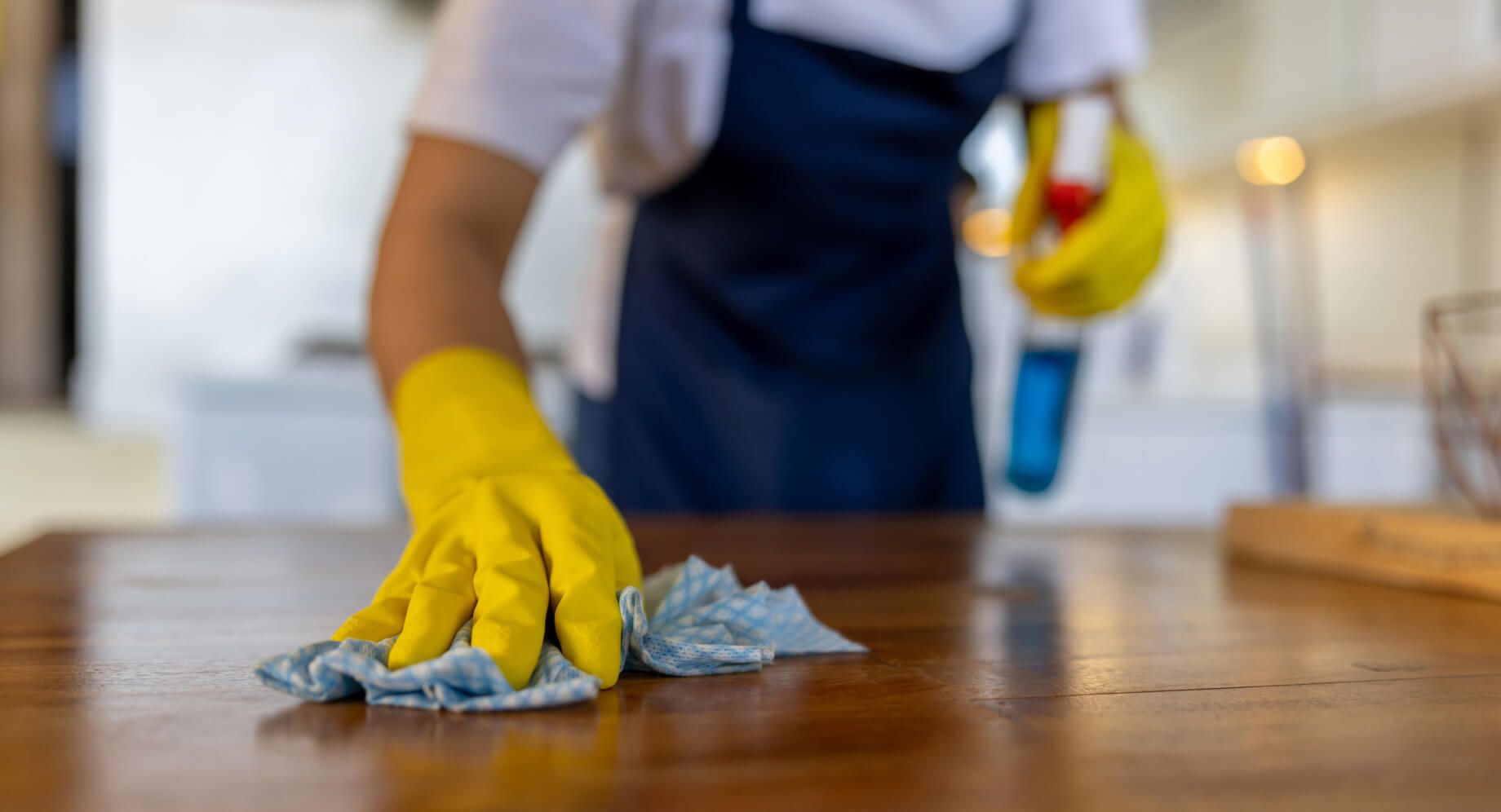 Person with rubber gloves cleaning table with cloth