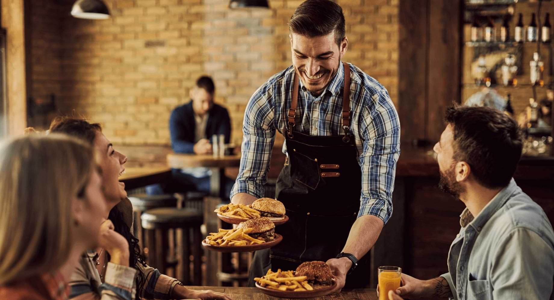 Smiling waiter serving restaurant guests plates of burgers and fries