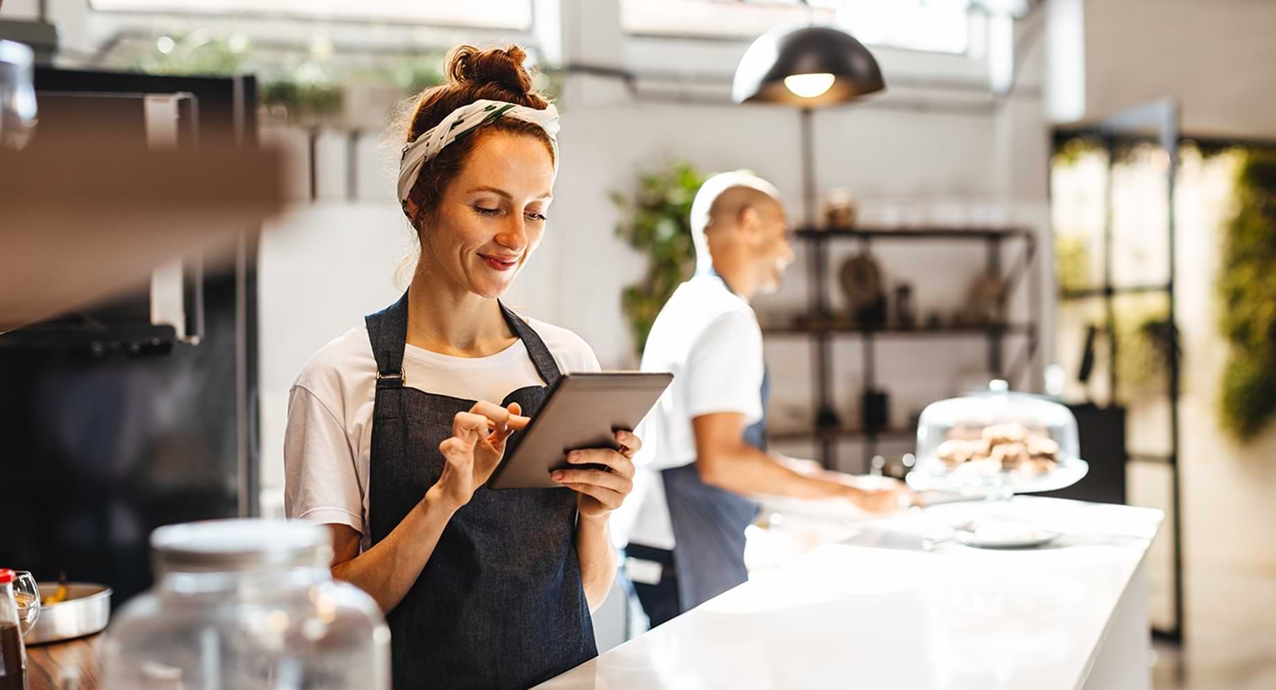 smiling woman behind bakery counter looking at digital tablet