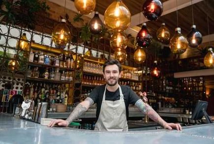 bartender leaning on counter smiling at camera inside upscale bar