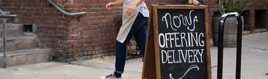 chalkboard outside of restaurant that has now offering delivery written in white