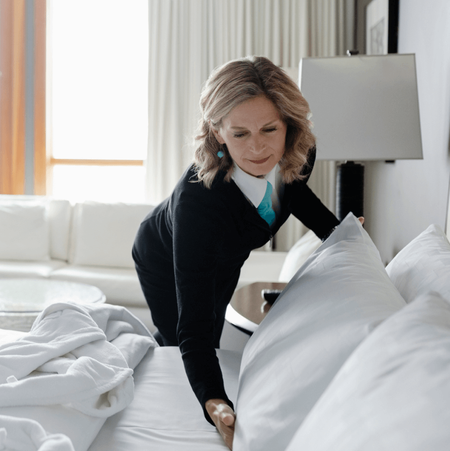Two hotel workers in uniforms turning down bed in hotel room