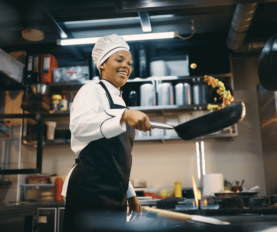 Happy chef wearing hat and apron tossing stir fry in pan